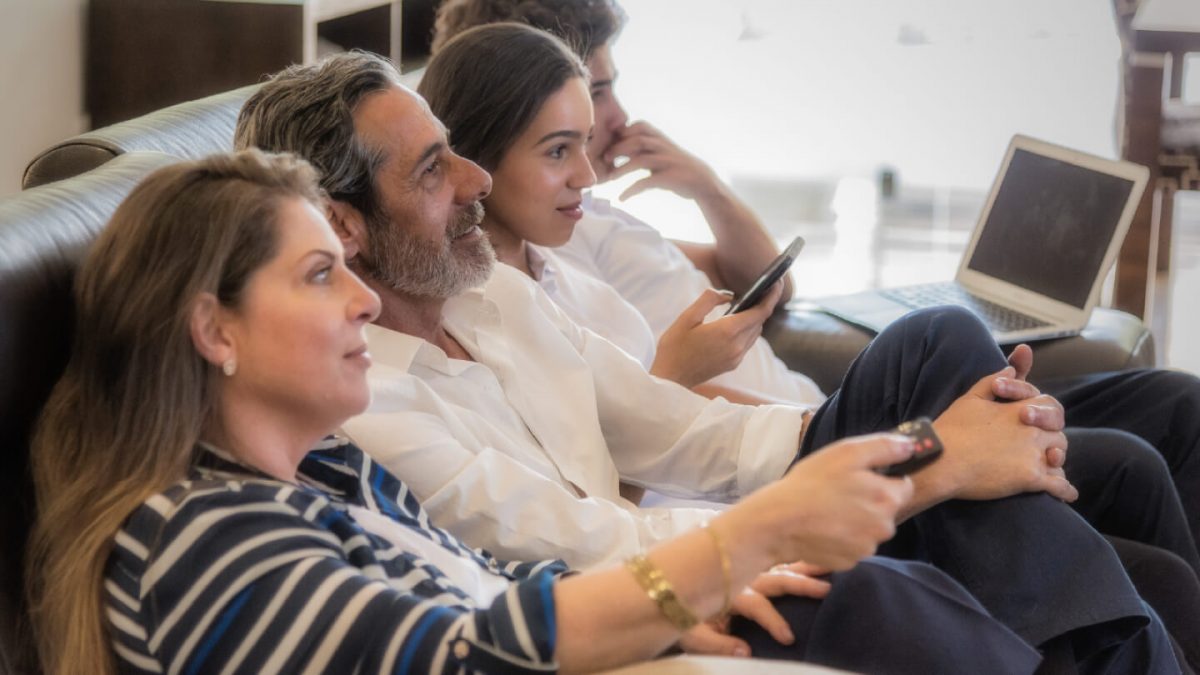 Photo: Family on couch with devices, watching TV — illustrates mobile campaigns benefit from CTV halo effect.