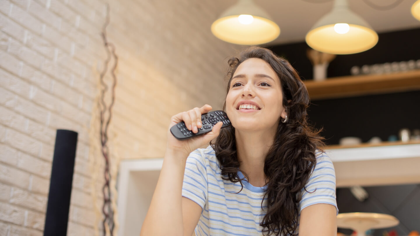 Stock photo: Joyful woman with remote — implies viewer engagement peaks when ads align with content.